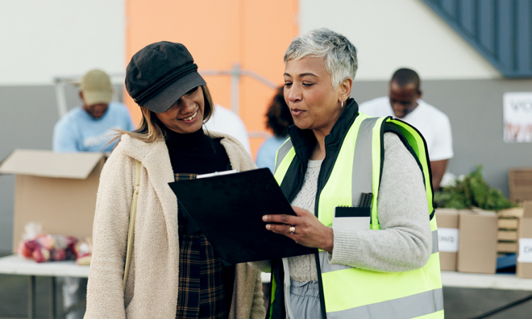 Person wearing safety vest talking to volunteer at food sort