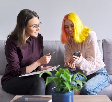 Teen girl with colourful hair talking to adult on couch