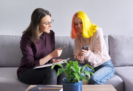 Teen girl with colourful hair talking to adult on couch