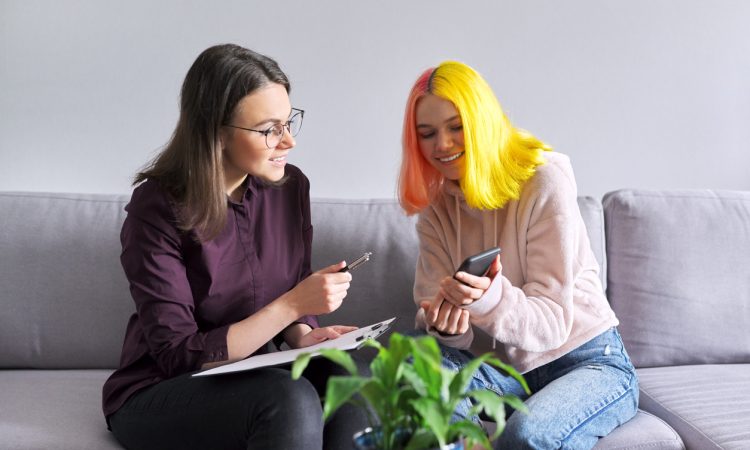 Teen girl with colourful hair talking to adult on couch