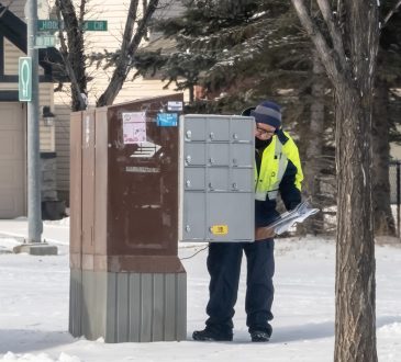 A postal worker depositing mail into a residential mailbox within the neighbourhood