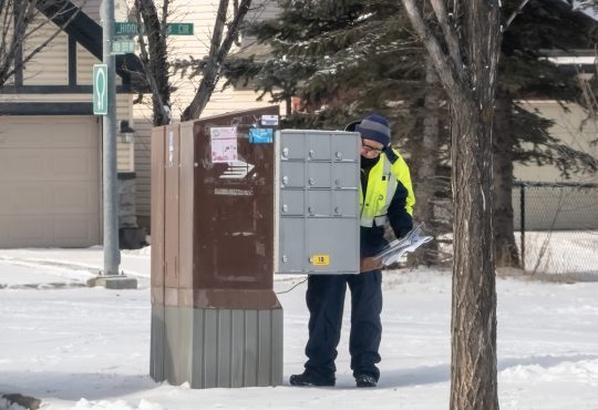 A postal worker depositing mail into a residential mailbox within the neighbourhood