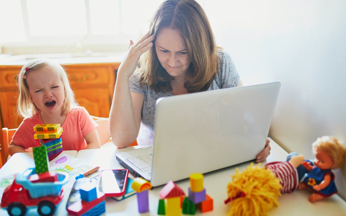 Stressed mom trying to work on computer at home beside screaming child