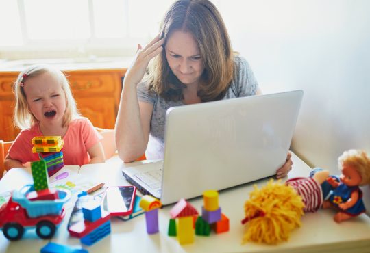 Stressed mom trying to work on computer at home beside screaming child