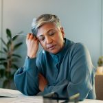 Stressed woman in office resting head on hand with eyes closed