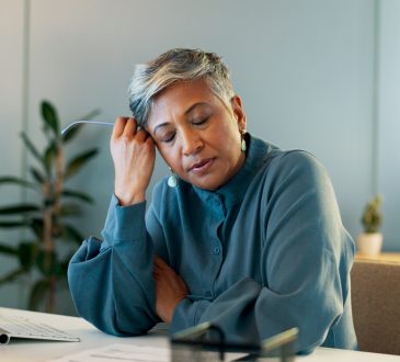 Stressed woman in office resting head on hand with eyes closed