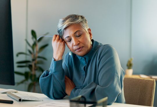 Stressed woman in office resting head on hand with eyes closed