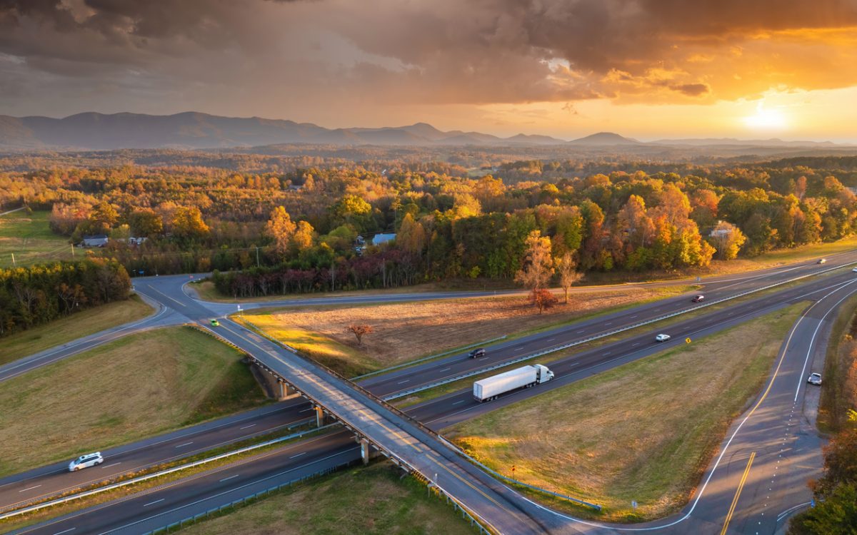 Freeway overpass junction with fast moving traffic cars and trucks in American rural area at sunset.