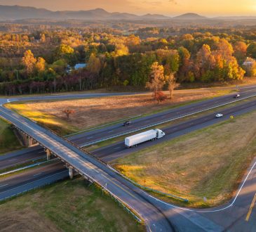 Freeway overpass junction with fast moving traffic cars and trucks in American rural area at sunset.