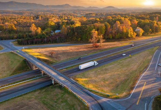 Freeway overpass junction with fast moving traffic cars and trucks in American rural area at sunset.