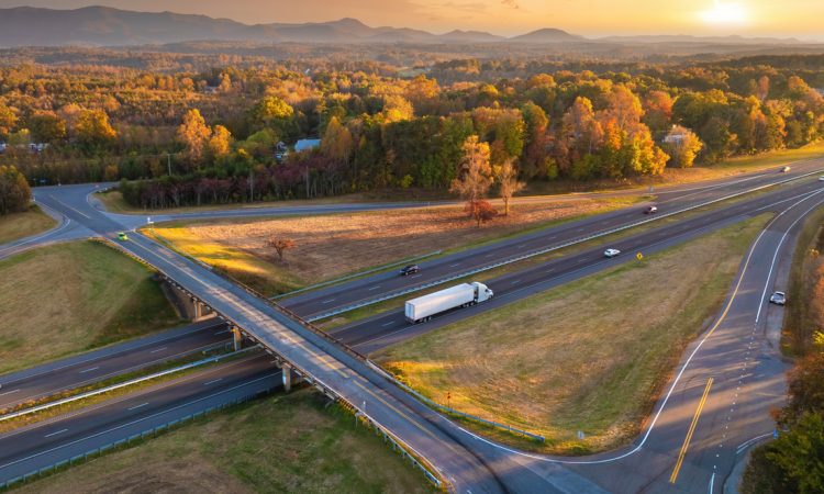 Freeway overpass junction with fast moving traffic cars and trucks in American rural area at sunset.