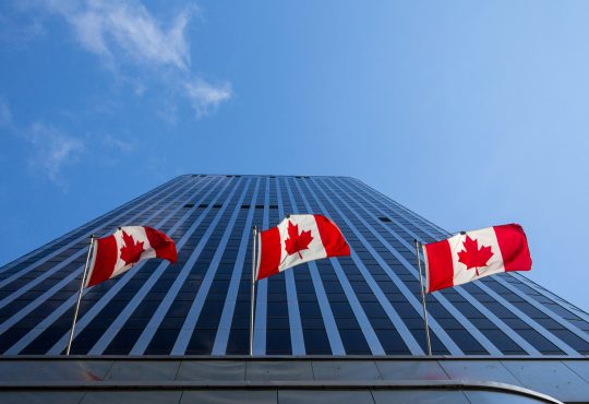 Three Canadian flags flying in front of business building in Ottawa