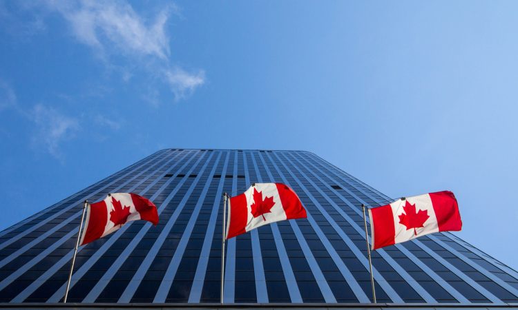 Three Canadian flags flying in front of business building in Ottawa
