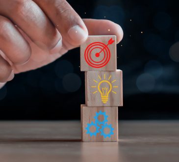 Closeup of hand stacking wooden blocks with icons of bullseye, lightbulb and gears