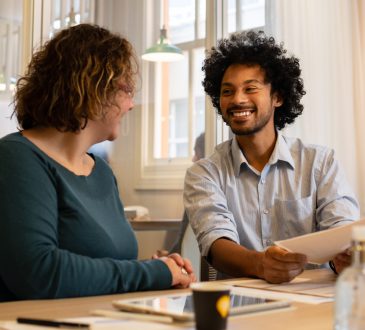 Man and woman chatting at table in office while looking at document together