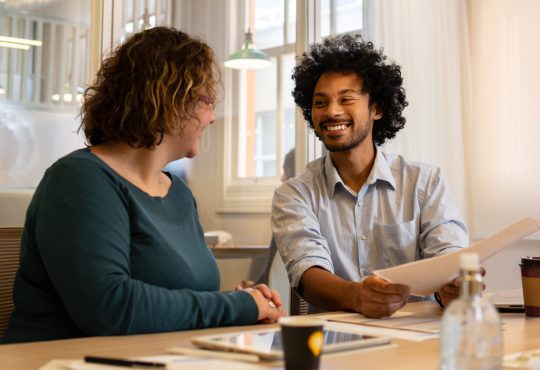 Man and woman chatting at table in office while looking at document together