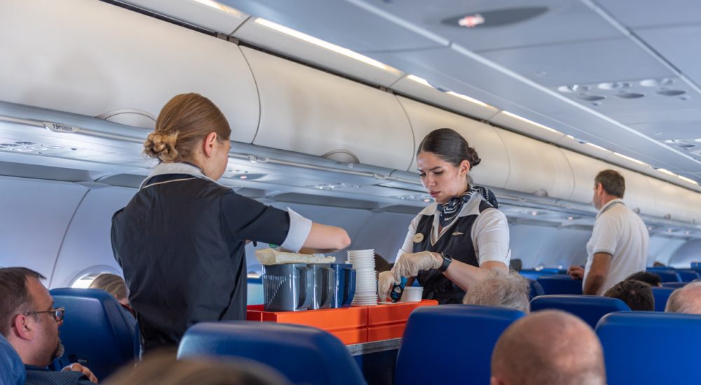 Two flight attendants with cart in airplane aisle