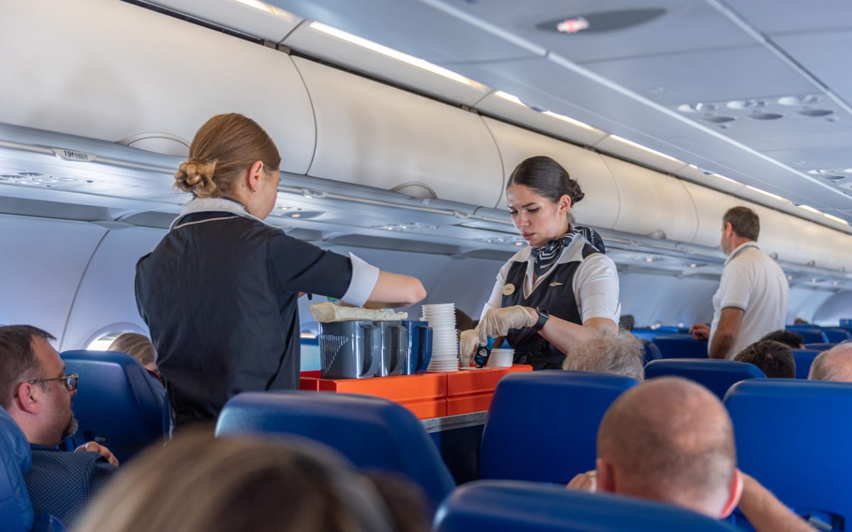 Two flight attendants with cart in airplane aisle