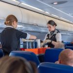 Two flight attendants with cart in airplane aisle