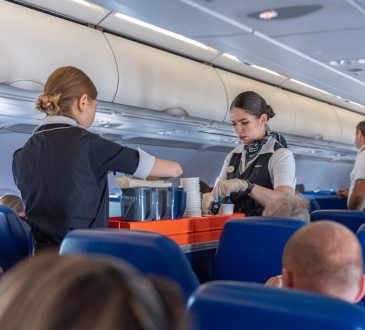 Two flight attendants with cart in airplane aisle