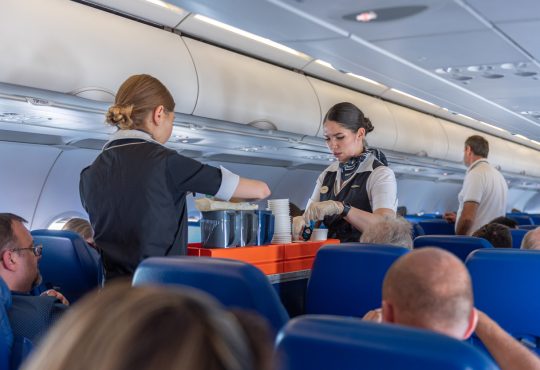 Two flight attendants with cart in airplane aisle