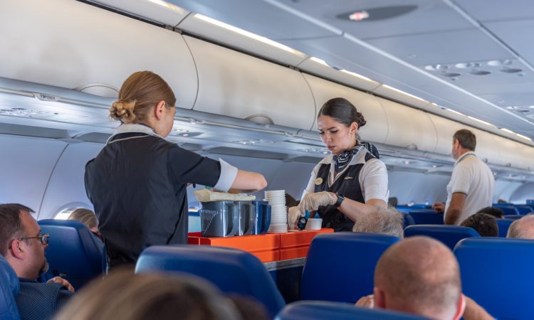 Two flight attendants with cart in airplane aisle