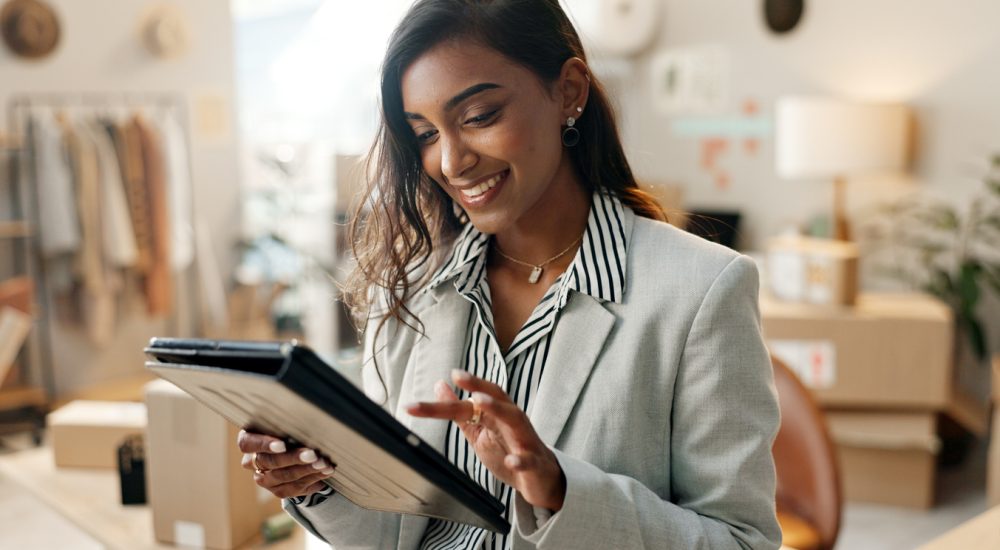 Woman standing looking at tablet in room with clothing racks and cardboard boxes