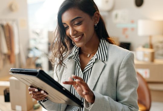 Woman standing looking at tablet in room with clothing racks and cardboard boxes