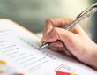 Hand ticking off checkmarks on list with pen attached to clipboard