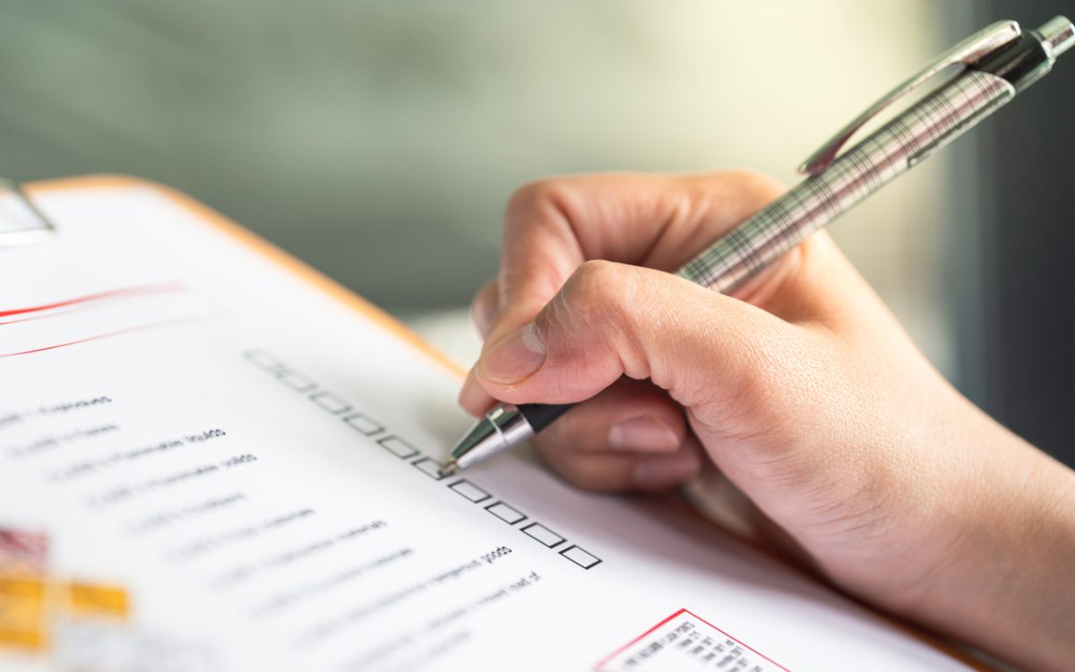 Hand ticking off checkmarks on list with pen attached to clipboard