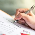 Hand ticking off checkmarks on list with pen attached to clipboard