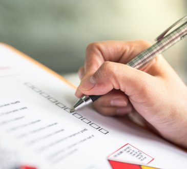 Hand ticking off checkmarks on list with pen attached to clipboard