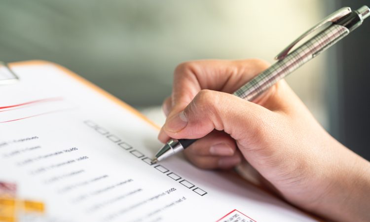 Hand ticking off checkmarks on list with pen attached to clipboard