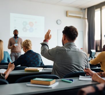 Rear view of man raising arm to ask a question during a presentation in lecture hall.