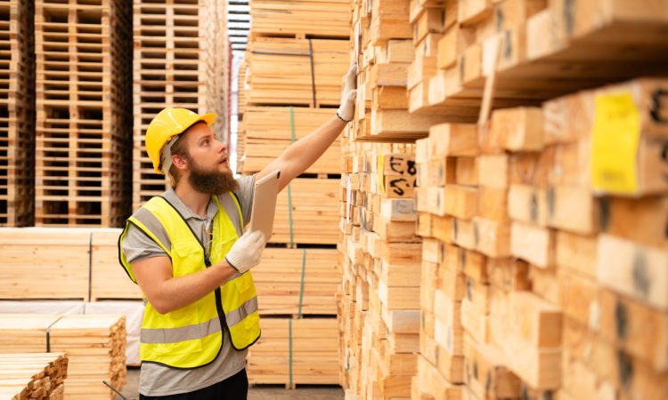 worker checking stock of wooden pallets in storage warehouse