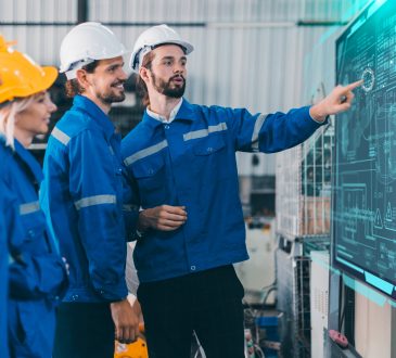 Team of engineers wearing hard hats looking at digital whiteboard together