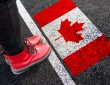a woman with a boots standing on asphalt next to flag of Canada and border
