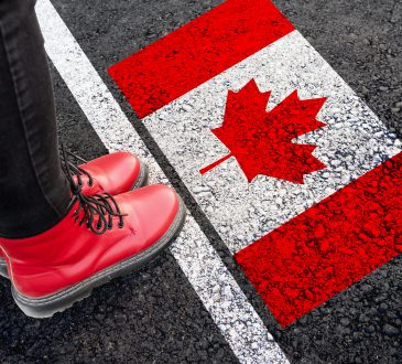 a woman with a boots standing on asphalt next to flag of Canada and border