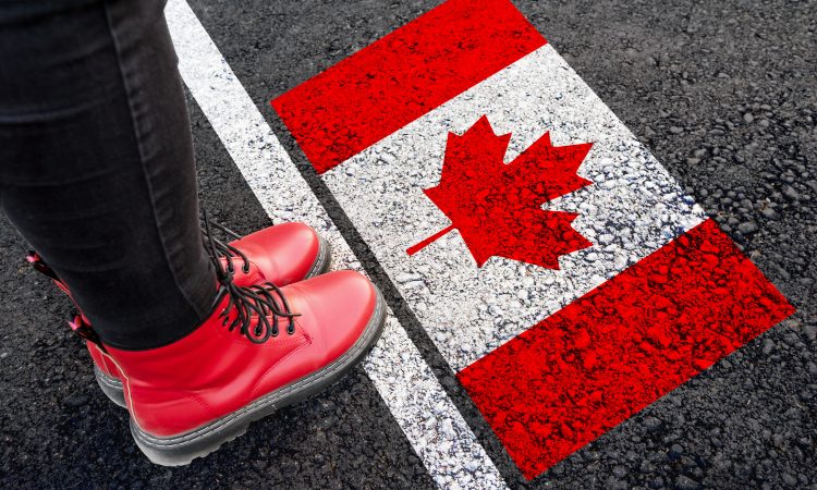a woman with a boots standing on asphalt next to flag of Canada and border