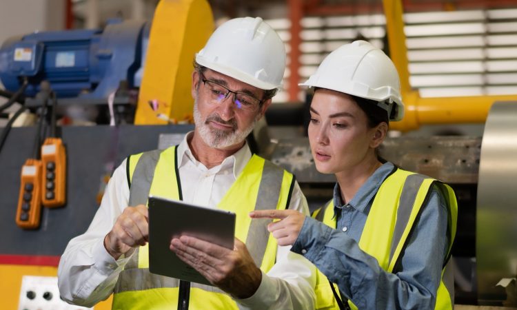 Senior manager on job training technician working in metal sheet production factory.