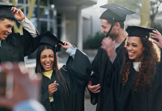 Group of graduates in caps and gowns celebrating outside