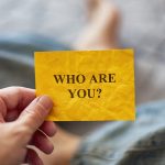 Man holding yellow paper note with question Who are you