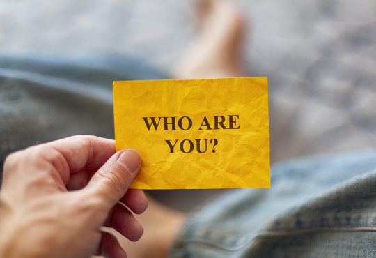 Man holding yellow paper note with question Who are you