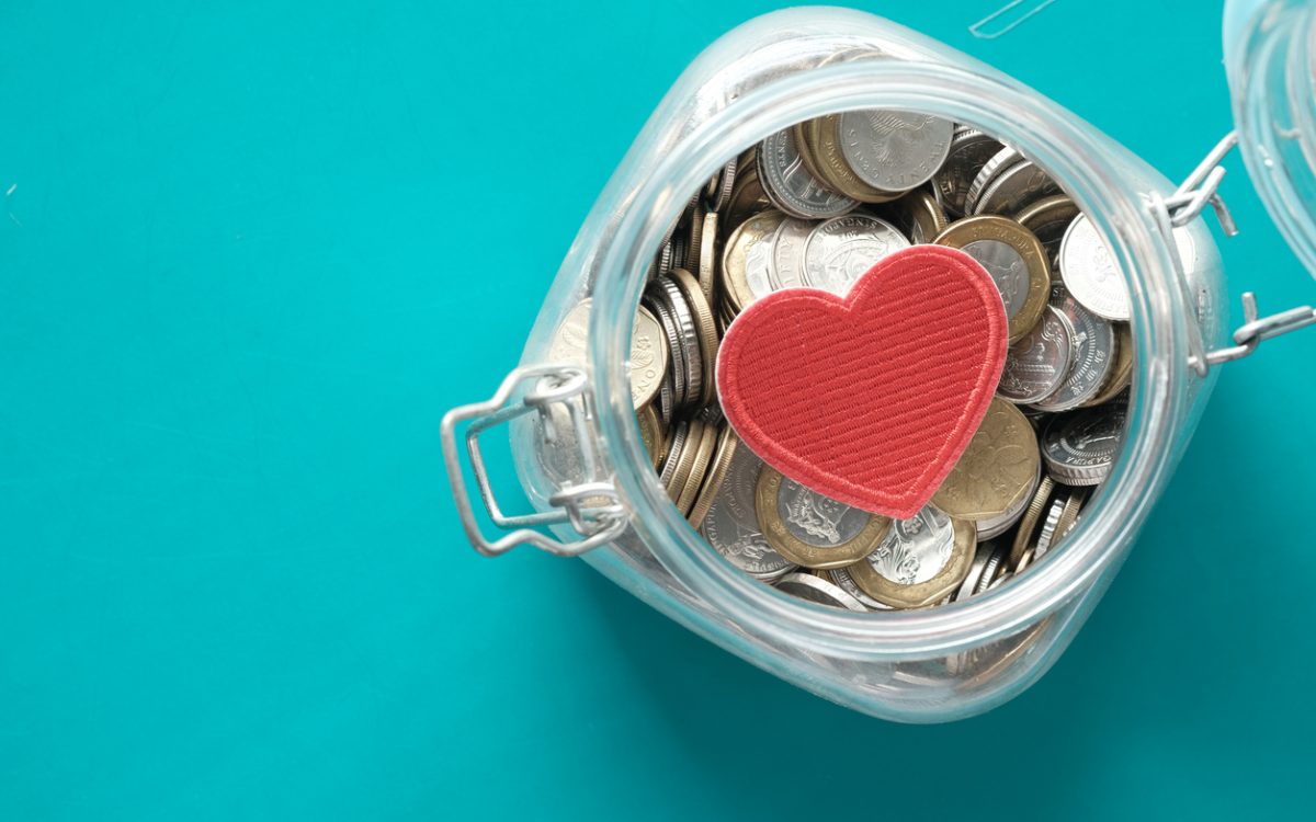 Red heart and coins in a jar on blue background .