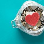 Red heart and coins in a jar on blue background .