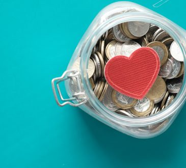 Red heart and coins in a jar on blue background .