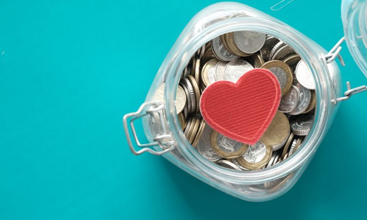 Red heart and coins in a jar on blue background .