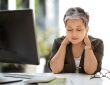 Woman sitting at desk with eyes closed, rubbing neck