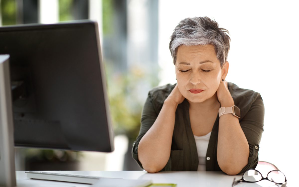 Woman sitting at desk with eyes closed, rubbing neck