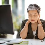 Woman sitting at desk with eyes closed, rubbing neck